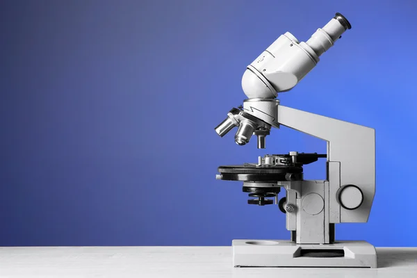 Mikroskop auf Tisch, auf blauem Hintergrund — Stockfoto