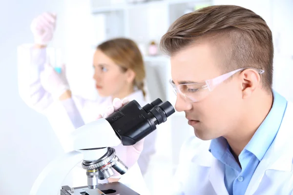 Científicas jóvenes y masculinas con microscopio en laboratorio — Foto de Stock