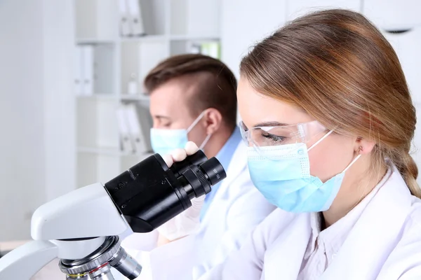Young female and male scientists  with microscope in laboratory — Stock Photo, Image