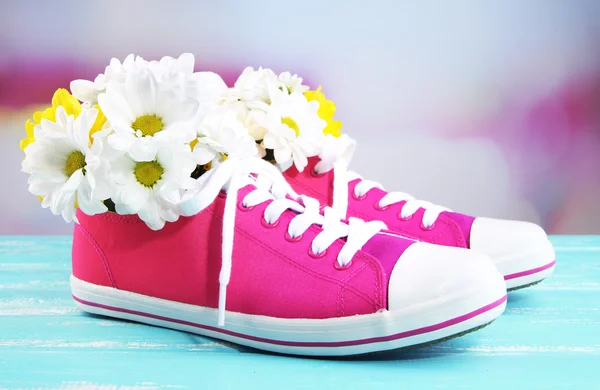 Vackra joggingskor med blommor inne på träbord, på ljus bakgrund — Stockfoto