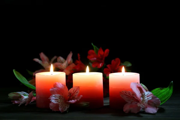 Beautiful candles with flowers on wooden table, on dark background — Stock Photo, Image
