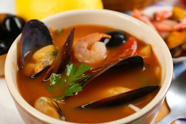 Tasty soup with shrimps, mussels, tomatoes and black olives in bowl on wooden background — Stock Photo, Image