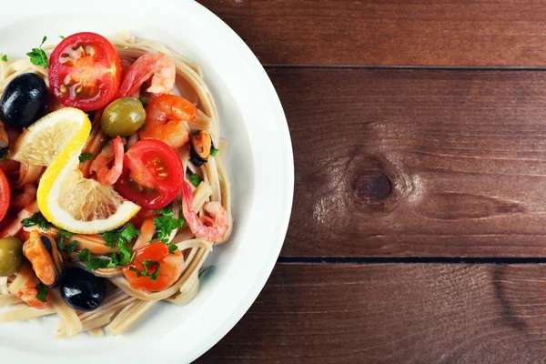 Tasty pasta with shrimps, mussels, black olives and tomato sauce on plate on wooden background — Stock Photo, Image