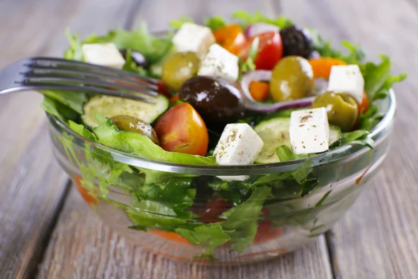 Salade grecque dans un plat en verre avec fourchette sur fond en bois — Photo