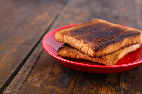 Burnt toast bread on red plate, on wooden table background — Stock Photo, Image