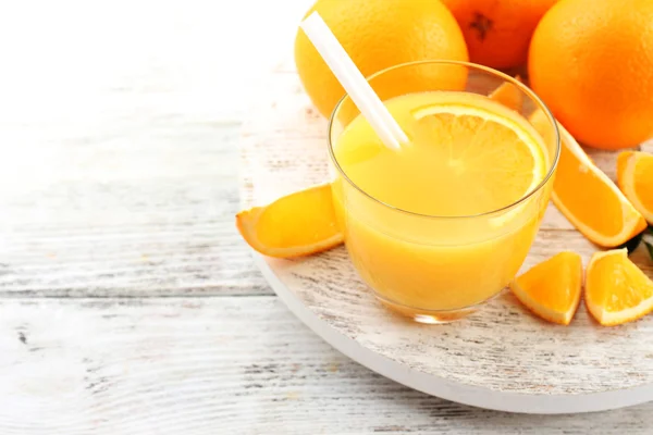 Copo de suco de laranja com palha e fatias em fundo de mesa de madeira — Fotografia de Stock