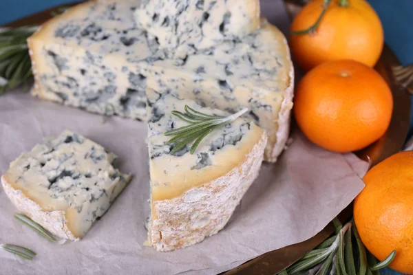 Blue cheese with sprigs of rosemary and oranges on metal tray with sheet of paper and color wooden table background — Stock Photo, Image