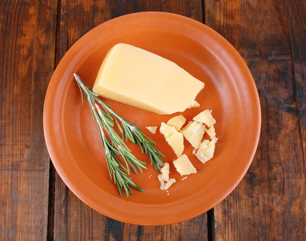 Parmesan cheese with sprig of rosemary on plate on wooden table background — Stock Photo, Image