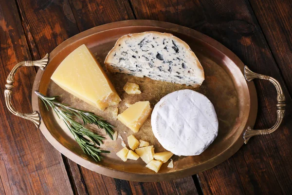 Different types of cheese on metal tray and wooden table background — Stock Photo, Image