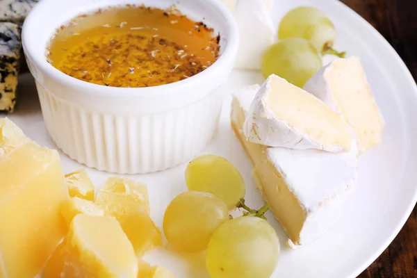 Diversi tipi di formaggio con uva e piattino su piatto su sfondo tavolo di legno — Foto Stock