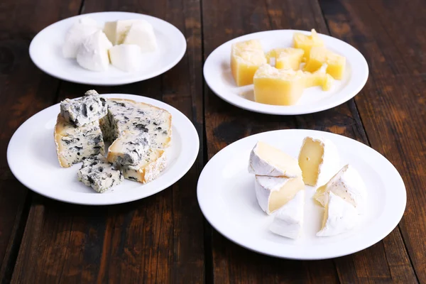 Vários tipos de queijo em placas no fundo da mesa de madeira — Fotografia de Stock