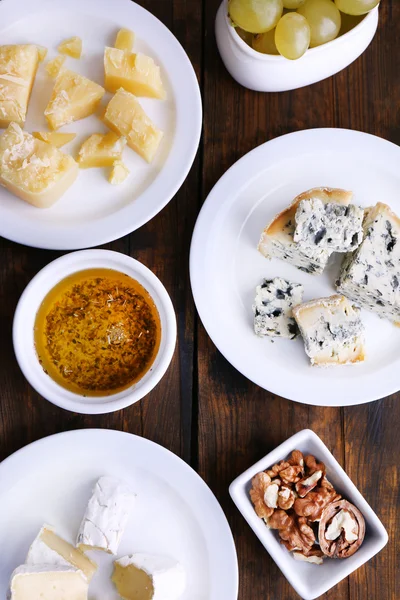 Différents types de fromage sur assiettes avec collations sur soucoupes sur fond de table en bois — Photo