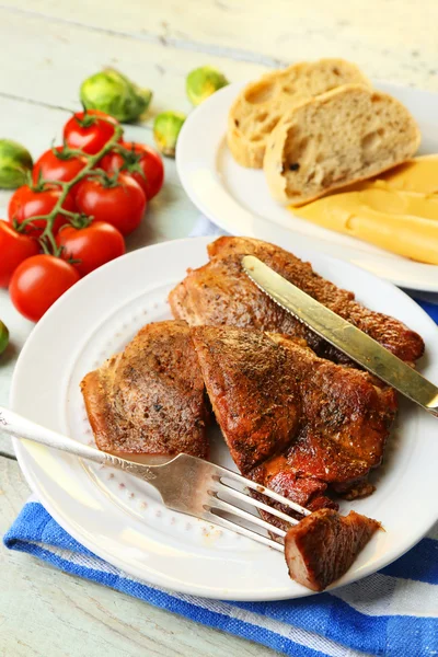 Roasted meat and vegetables on plate, on wooden table background — Stock Photo, Image