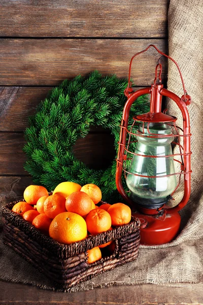 Petroleumlampe mit Kranz und Orangen im Weidenkorb auf Holzplanken Hintergrund — Stockfoto