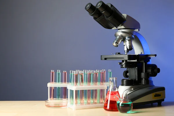Микроскоп и пробирки на столе, на цветном фоне — стоковое фото
