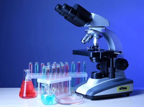 Microscope and test tubes on table, on color background — Stock Photo, Image