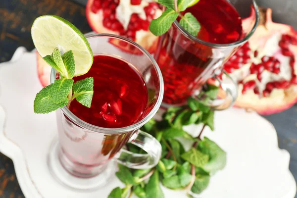 Pomegranate drink in glasses with mint and slices of lime on plate and color wooden background — Stock Photo, Image