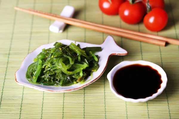 Insalata di alghe in piatto su sfondo tappetino di bambù — Foto Stock