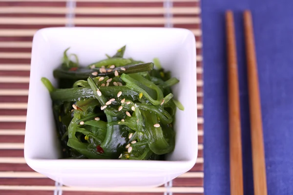 Seaweed salad in bowl with sticks on bamboo mat and color table background — Stock Photo, Image