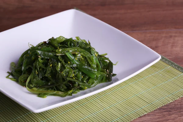 Salade d'algues en assiette sur tapis de bambou et fond de table en bois — Photo