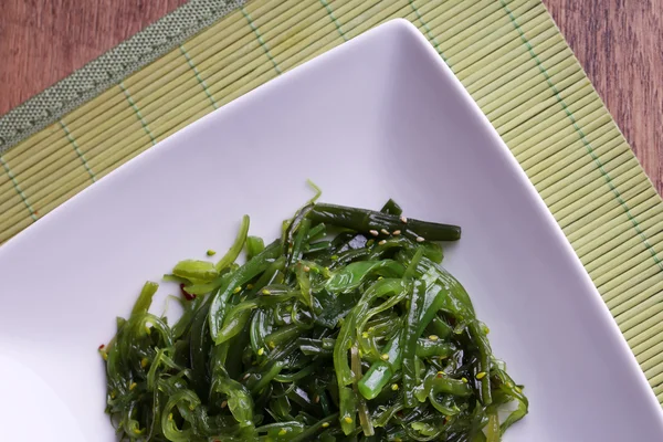 Ensalada de algas marinas en plato sobre estera de bambú y fondo de mesa de madera — Foto de Stock