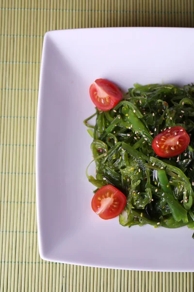 Insalata di alghe con fette di pomodoro ciliegia su sfondo tappetino di bambù — Foto Stock