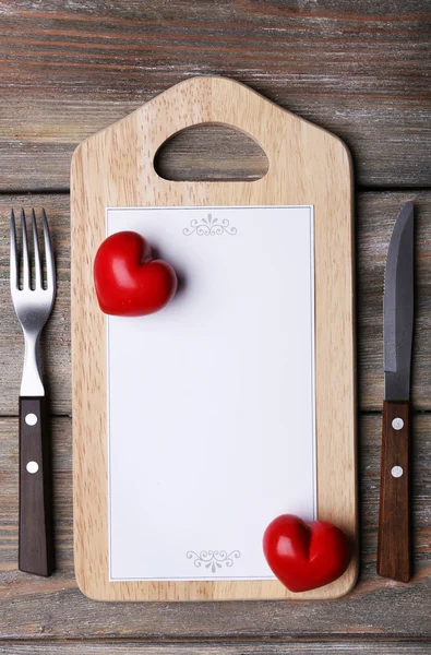 Cutting board with menu sheet of paper and hearts on rustic wooden planks background — Stock Photo, Image