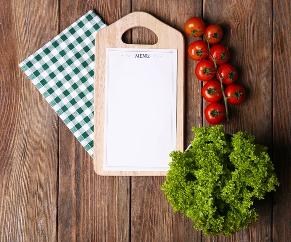 Cutting board with menu sheet of paper, with cherry tomatoes and lettuce on wooden planks background — Stock Photo, Image