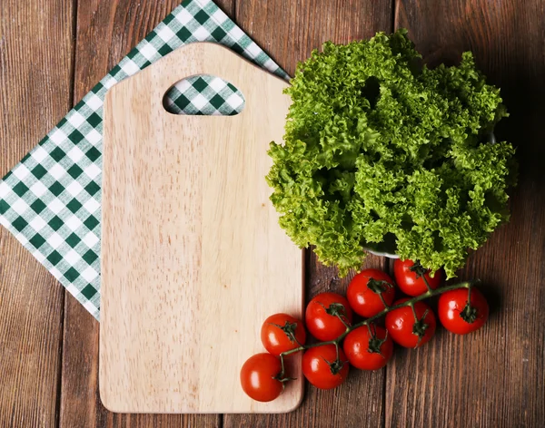 Cutting board with cherry tomatoes and lettuce on wooden planks background — Stock Photo, Image