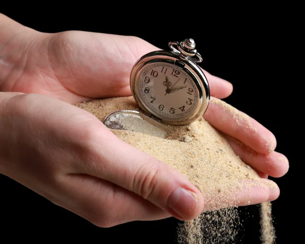 Horloge de poche argentée dans les mains et le sable s'écoulant sur fond noir — Photo