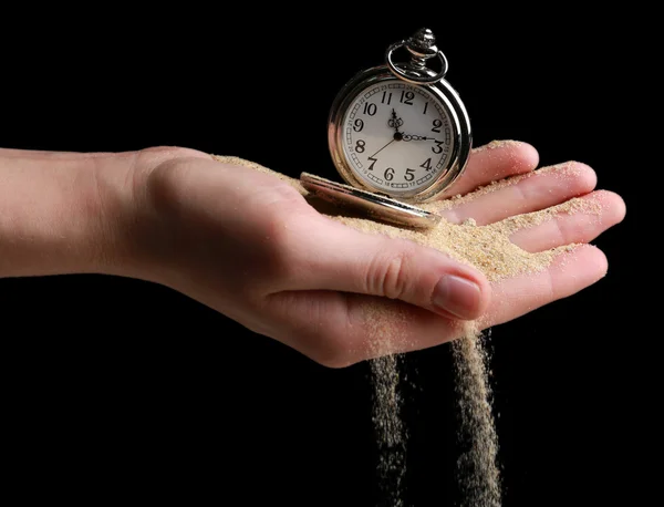 Reloj de bolsillo de plata en las manos y la arena que fluye sobre fondo negro —  Fotos de Stock