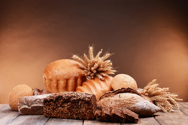 Pão diferente na mesa no fundo marrom — Fotografia de Stock