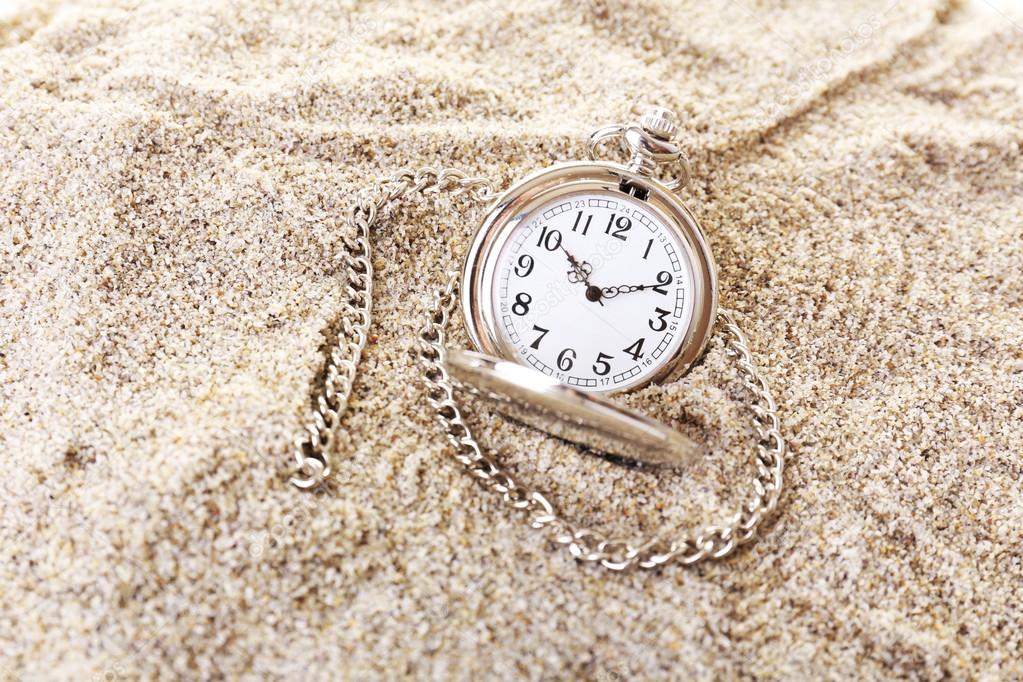 Silver pocket clock on sand background