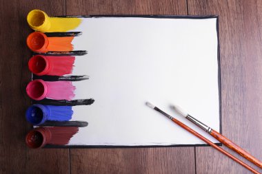 Renkli boya konturları fırça ve boya kutular ahşap masa arka plan üzerinde beyaz kağıda ile