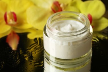 Koyu arka plan üzerinde orkide çiçekli yüz kremi