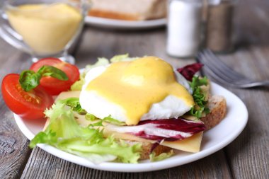 Yumurta Benedict ile tost ve ahşap masa üzerinde tabakta domates