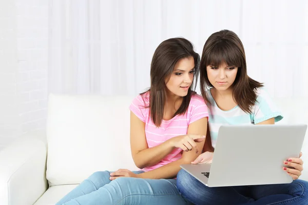 Belle ragazze gemelle sedute sul divano con notebook — Foto Stock