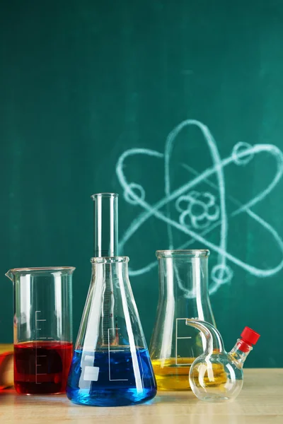 Стол в классе химии с пробирками на зеленом фоне доски — стоковое фото