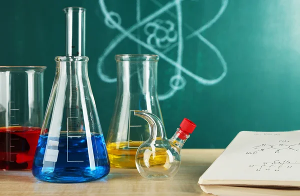 Schreibtisch im Chemieunterricht mit Reagenzgläsern auf grünem Tafel-Hintergrund — Stockfoto