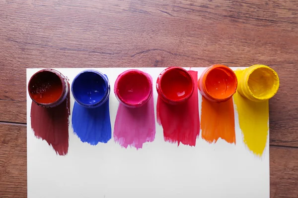 Kolorowe farby ruchami i puszki farby na białą kartkę papieru na drewnianym stole tło — Zdjęcie stockowe