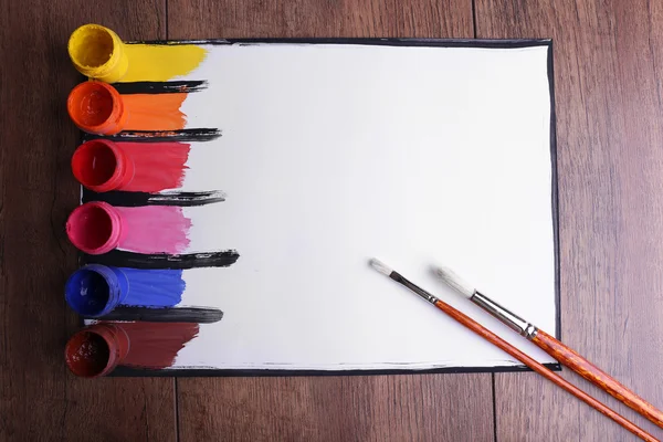 Kleurrijke penseelstreken met penseel en verf blikjes op wit vel papier op houten tafel achtergrond — Stockfoto