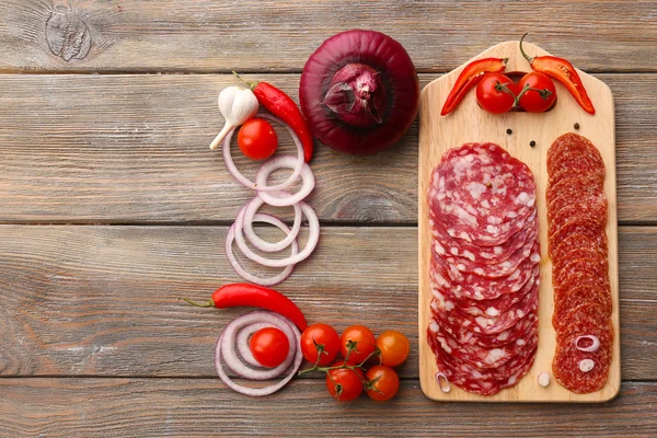 Salame affettato con peperoncino, pomodorini ciliegini, cipolla e spezie su tagliere e fondo tavola in legno — Foto Stock