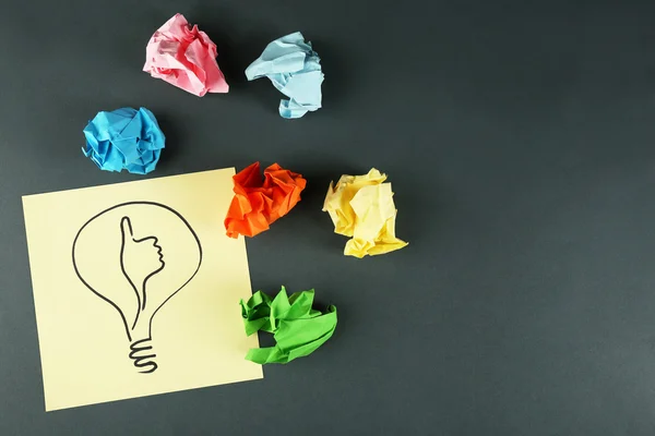 Symbol of idea as light bulb on sheet of paper with crumpled paper on color table background — Stock Photo, Image