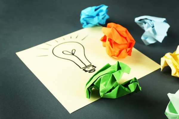 Symbol of idea as light bulb on sheet of paper with crumpled paper on color table background — Stock Photo, Image