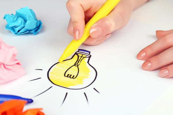 Female hand drawing symbol of idea as light bulb on sheet of paper, on white background — Stock Photo, Image