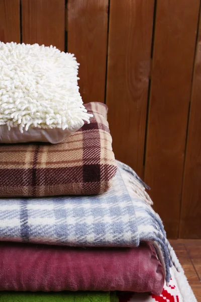 Mucchio di plaid caldi e cuscino su sfondo in legno rustico — Foto Stock