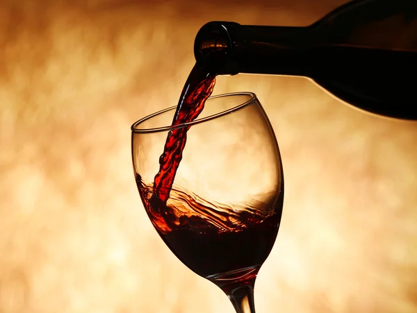 Pouring red wine from bottle into glass on color background — Stock Photo, Image