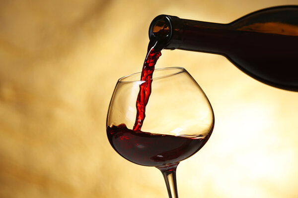 Pouring red wine from bottle into glass on color background