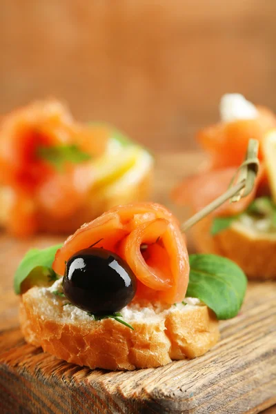 Tartine con salmone, olive nere ed erbe aromatiche su tagliere, su fondo di legno — Foto Stock