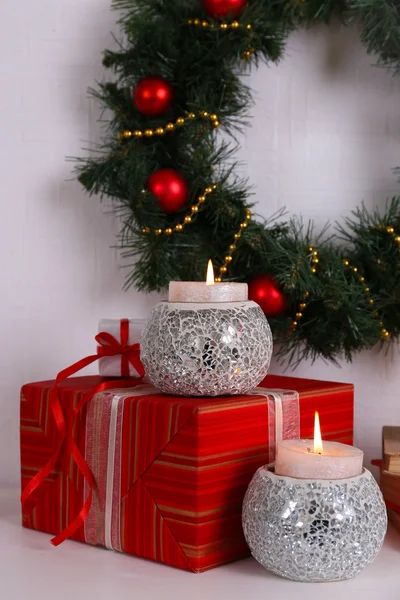 Kerstdecoratie met krans, kaarsen en huidige vakken op plank op witte muur achtergrond — Stockfoto